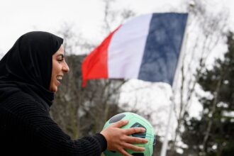 امرأة مبتسمة تحمل كرة قدم خضراء.