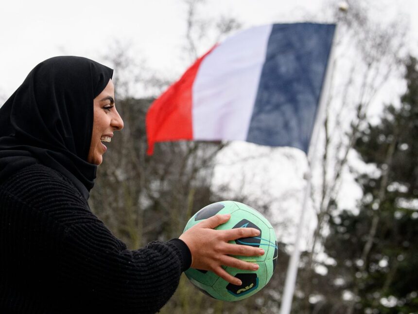 امرأة مبتسمة تحمل كرة قدم خضراء.