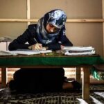 امرأة تجلس على الأرض وتحمل قلماً وتنظر إلى كتاب