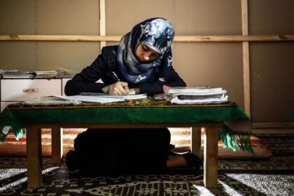 امرأة تجلس على الأرض وتحمل قلماً وتنظر إلى كتاب