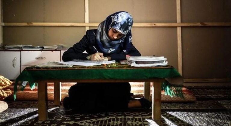 امرأة تجلس على الأرض وتحمل قلماً وتنظر إلى كتاب
